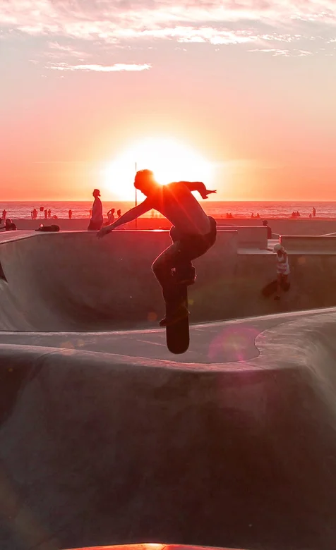 夕阳下的沙滩场地玩滑板运动员们手机壁纸