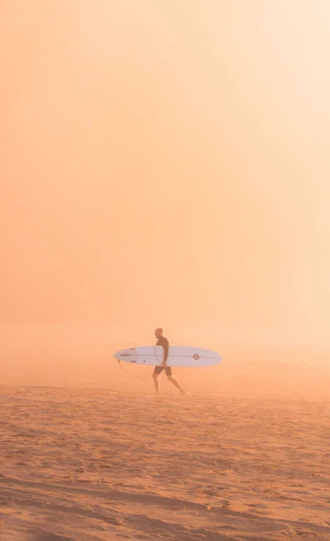 大雾笼罩的沙滩，抱着冲浪板走过的欧美男士手机壁纸
